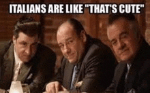 three men in suits are sitting at a table with a caption that says `` italians are like that 's cute '' .