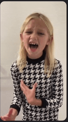 a little girl in a black and white sweater is making a funny face with her mouth open .