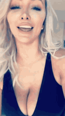 a blonde woman in a black tank top is smiling with her mouth open