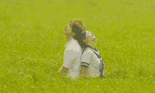 a man and a woman are sitting back to back in a grassy field looking up at the sky .