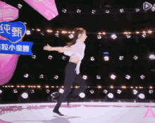 a woman in a white shirt and black pants is running on a stage