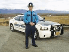 a police officer is standing in front of a police car on a dirt road .