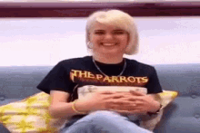 a woman wearing a t-shirt that says the parrots is sitting on a couch .