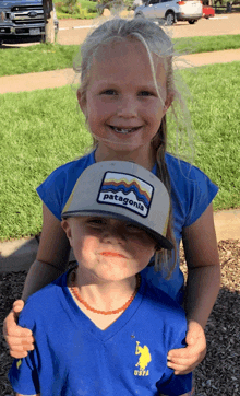 a little girl wearing a patagonia hat is holding a little boy