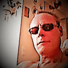 a man wearing sunglasses looks at the camera with a serious look on his face .