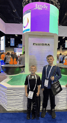 two young boys are standing in front of a sign that says fluidra