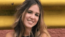 a woman with long hair is smiling for the camera in front of a yellow and red wall .