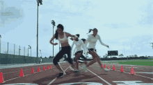 a group of women are running on a track and one of them is wearing a white tank top .