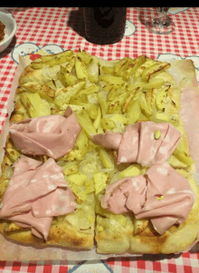 a pizza with potatoes and meat on it on a checkered table cloth