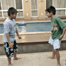 two young boys standing in front of a swimming pool one of whom is wearing a shirt that says ' rump '