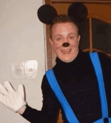 a man in a mickey mouse costume is wearing blue suspenders and white gloves .