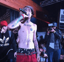 a shirtless man singing into a microphone wearing an adidas sweatshirt