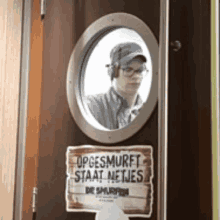 a man wearing headphones is looking through a round window with a sign that says opgesmurft staat metjes