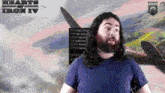 a man with long hair and a beard stands in front of a screen that says " hearts of iron iv "