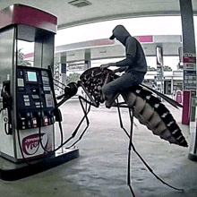 a man is sitting on a mosquito in front of a gas pump that says jetmaster