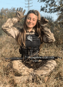 a woman in a military uniform is kneeling in the grass with a gun