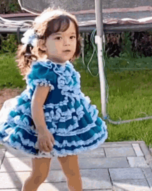 a little girl in a blue and white dress is standing on a sidewalk in front of a trampoline .