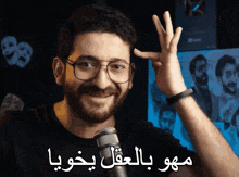 a man with glasses and a beard is smiling in front of a microphone with arabic writing behind him