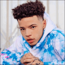 a young man with curly hair is wearing a blue and white tie dye hoodie and earrings .