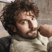 a man with curly hair and a beard is sitting in a chair and looking at the camera .