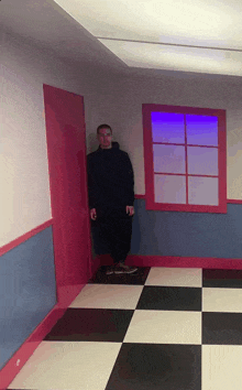 a man in a black hoodie stands in a room with a checkered floor