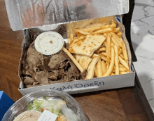 a box of gyros and french fries sits on a table next to a plastic container of salad