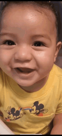 a close up of a baby wearing a yellow mickey mouse shirt smiling .