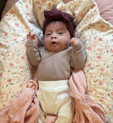 a baby wearing a headband is laying on a blanket with flowers on it