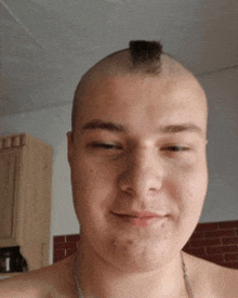 a shirtless man with a mohawk on his head looks at the camera