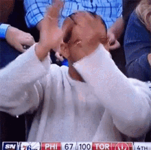 a man in a white shirt is sitting in a stadium watching a basketball game between phillies and toronto raptors