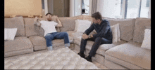 two men are sitting on a couch in a living room talking