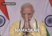 a man with a beard is praying in front of a flag with the word namaskar written on it .