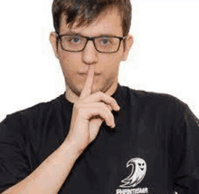 a man wearing glasses and a black shirt is covering his mouth with his finger .