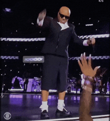 a man in a suit and shorts is dancing on a stage with a cbs logo in the corner