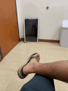 a person wearing flip flops is sitting on a tiled floor next to a trash can