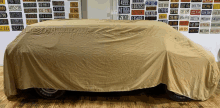 a car is covered with a tan cover and a wall of license plates