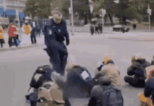 a group of people are sitting on the ground on the side of a street while a man in a helmet is running across the street