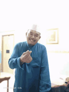 a man wearing a blue shirt and a white hat is smiling and giving a heart sign