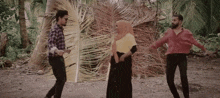 a woman in a hijab is dancing with two men in a field