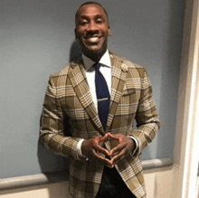 a man in a plaid suit and tie is smiling while standing in front of a blue wall .