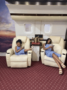 two little girls are sitting in chairs with their legs crossed and looking at their phones