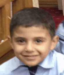 a young boy in a blue shirt and tie is smiling