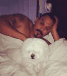 a man laying in bed with a white dog