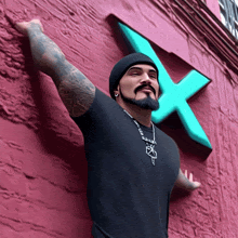 a man wearing a black shirt and a beanie stands in front of a large x on a pink wall