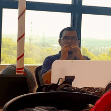 a man wearing glasses sits at a desk in front of a laptop