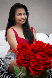 a woman is sitting on a couch with a bouquet of red roses in front of her