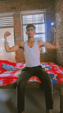 a man in a white tank top is sitting on a bed