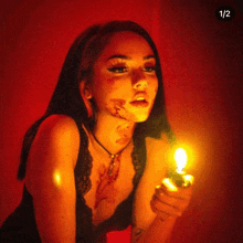 a woman with blood on her face is holding a candle with the number 1/2 below it