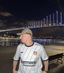 a man standing in front of a bridge wearing a barmenia shirt