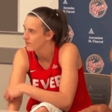 a female basketball player wearing a red jersey with the word ever on it is sitting at a table .